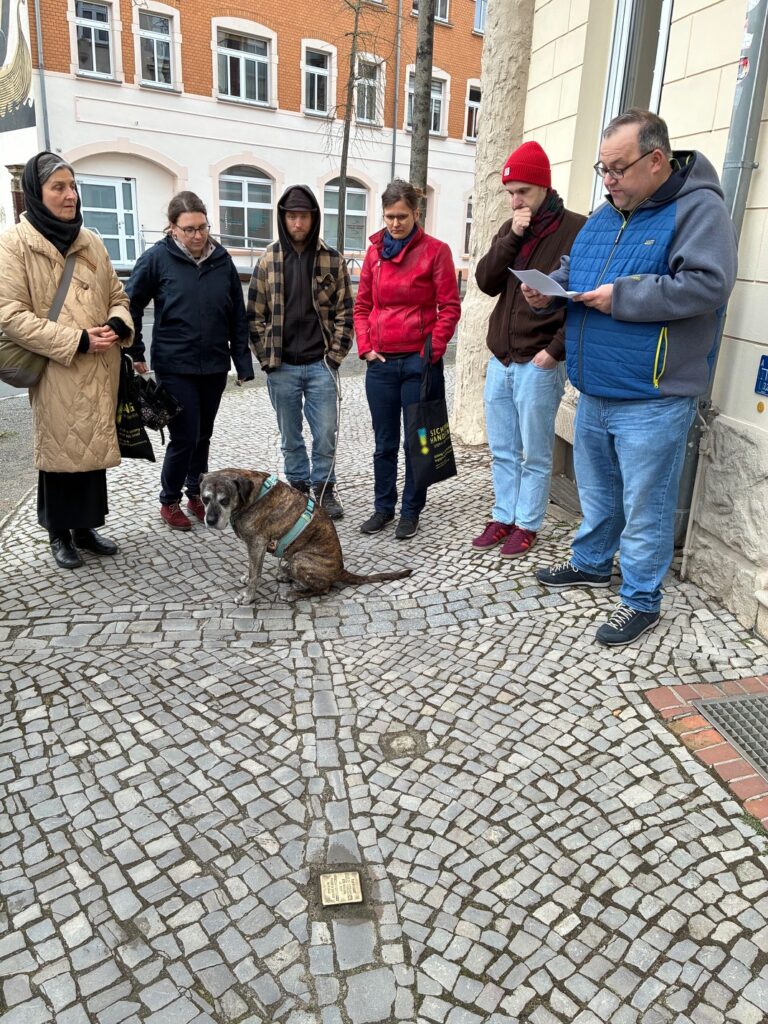 Eine KLeingruppe steht um einen Stolperstein, der im Boden eingelassen ist, und verliest Informationen dazu.